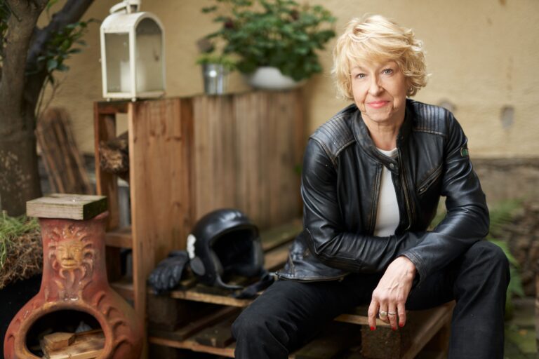 Maria Lahmann in Motorrradkleidung aus Leder, neben sich einen Helm